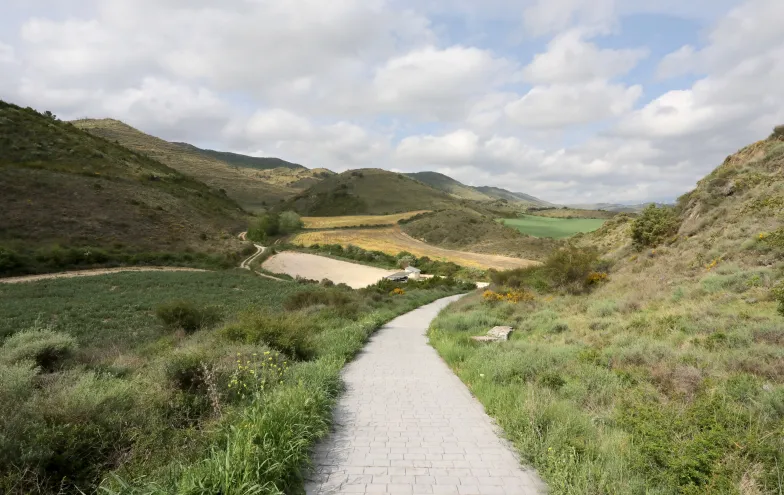 Sendero pavimentado atraviesa valle con montañas y cultivos, en los alrededores de Eslava.