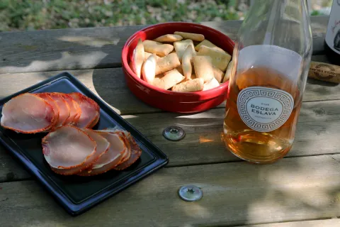 Degustación de productos locales en Bodega Eslava con lomo, pan y vino rosado sobre mesa de madera.