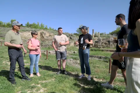 Grupo de visitantes degustando vino de la Bodega Eslava con yacimiento de Santa Criz de Eslava al fondo.