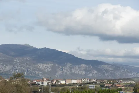 Etxarri Aranaz al pie de la sierra, con montañas al fondo y cielo nuboso en la composición panorámica.
