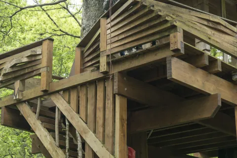escaleras y plataforma de madera, donde dos turistas suben una cesta de mimbre mediante una polea.
