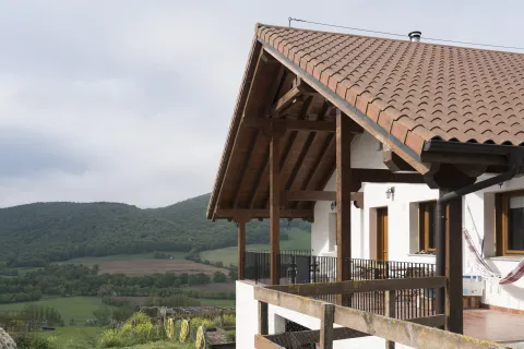 Porche de madera y vistas al valle de Ultzama, con prados verdes y monte boscoso.