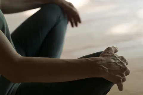 Detalle de manos sobre las rodillas de persona sentada practicando yoga en la experiencia de Ekino Aukera.