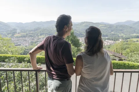 huespedes contemplan el Valle de Baztan desde un balcon de Markulluko Borda, con pueblo de Elizondo y montes verdes al fondo.
