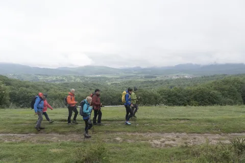 Grup de personas caminan en esplanada verde con bosque y monte al fondo, experiencia turistica de Lorentx.