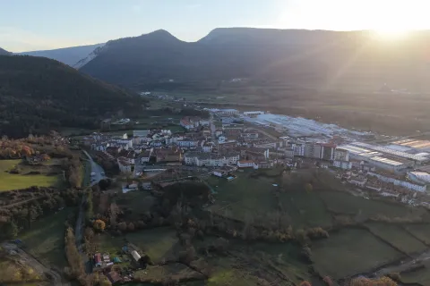 Vista aérea de Irurtzun con montañas al fondo, pueblo rodeado de bosques y prados.
