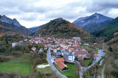 Vista aérea de Isaba rodeada de montes boscosos y cimas rocosas, pueblo pirenaico en valle con arquitectura tradicional.