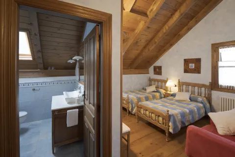 habitación rústica con techos de madera, dos camas de madera y baño en alojamiento rural en Isaba, Pirineo de Navarra.