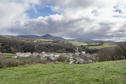 Pueblo de Lantz rodeado de prados verdes y bosques con montañas al fondo bajo cielo nublado.