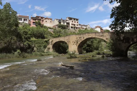 Puente de piedra sobre río en Lumbier, con pueblo en ladera y vegetación.
