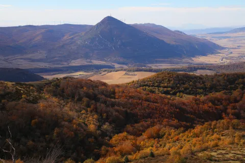 Vista panorámica del valle con la Higa de Monreal y bosque en otoño al fondo bajo cielo despejado.