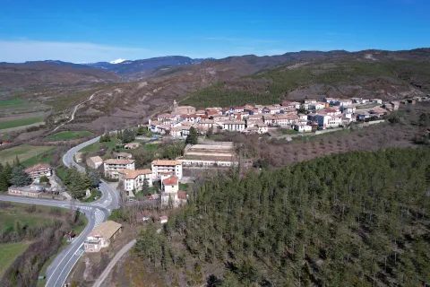Vista aérea de Navascués rodeado de bosques y montañas del Pirineo navarro con carretera de acceso.