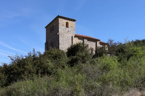 Ermita románica de Santa María de Arce en el Pirineo navarro, iglesia de piedra con torre campanario cuadrada sobre vegetación de transición.