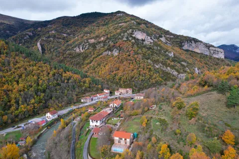 Vista aérea de Urzainqui con casas dispersas en valle pirenaico rodeado de bosque en otoño y acantilados de roca caliza.
