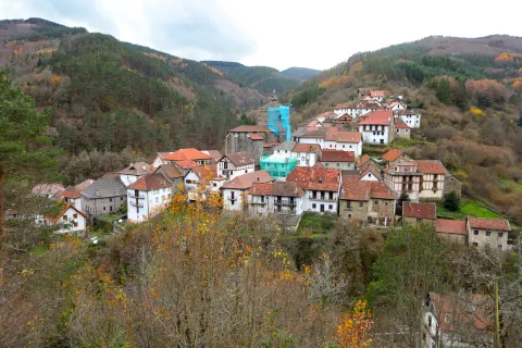 Pueblo de Uztarroz en valle pirenaico con casas tradicionales de tejados rojos, iglesia de piedra y bosques de montaña al fondo en otoño.