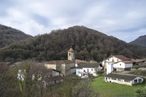Iglesia con torre campanario de piedra de Anue en entorno de monte verde con casas dispersas.