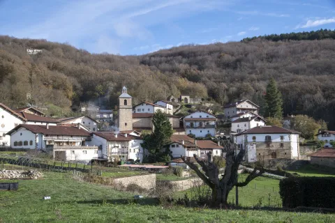 Pueblo de Imoz con iglesia campanario y casas de piedra blanca rodeado de bosques montañosos de robles.