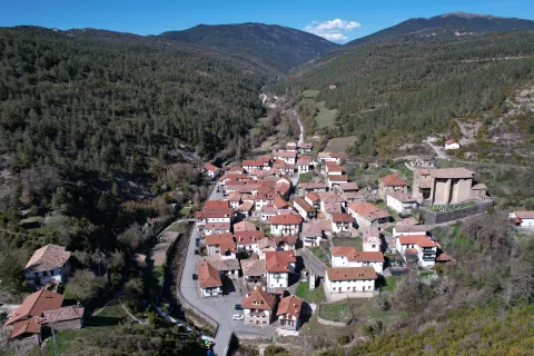 Vista aerea del pueblo de Vidangoz rodeado de bosques pirenaicos, con casas de tejado rojo y valle verde al fondo.
