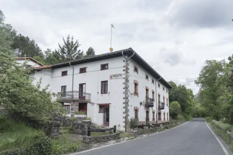 Casa tradicional de Zandueta con fachada blanca y balconada de hierro en entorno boscoso.