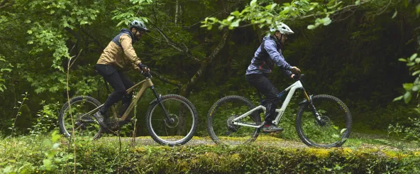 Dos ciclistas en sendero BTT entre bosque atlántico con arroyo y puente con musgo en Lesaka, Baztan-Bidasoa.