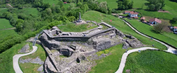 Ruinas del castillo de Amaiur en valle verde de Baztan, con muros de piedra y monumento conmemorativo.