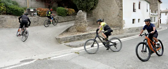 Grupo de ciclistas en ruta por las calles de piedra del territorio Eslava, con arquitectura tradicional al fondo.