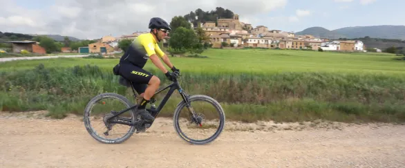 Ciclista en ruta de bicicleta eléctrica en Eslava con pueblo medieval al fondo y valle verde.
