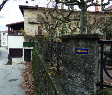 Calle de pueblo con arquitectura rural tradicional, flecha azul de Camino de Santiago, muros de piedra 