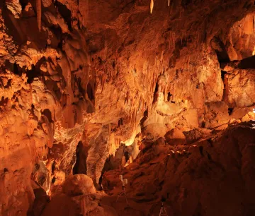 Cuevas de Mendukilo por dentro, con estalactitas y estalacmitas alumbradas con luces anaranjadas.