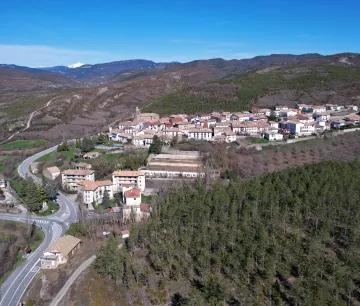 Vista aérea de Navascués rodeado de bosques y montañas del Pirineo navarro con carretera de acceso.
