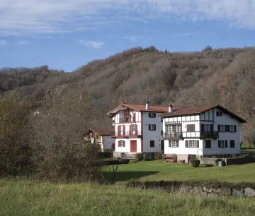 Tres casas tradicionales de Etxalar rodeadas de prados verdes y montes.