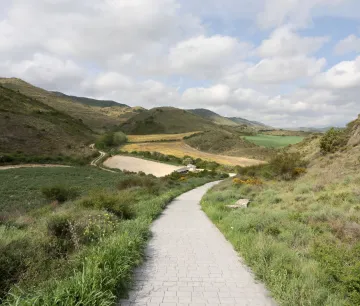 Sendero pavimentado atraviesa valle con montañas y cultivos, en los alrededores de Eslava.