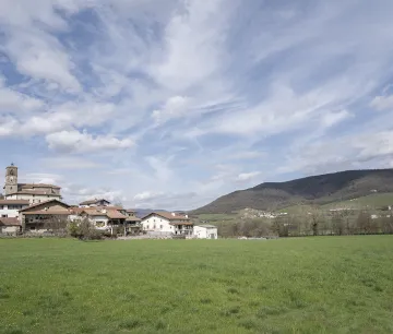 Pueblo del Valle de Ultzama con iglesia de campanario, caseríos tradicionales y prado verde bajo cielo nublado.