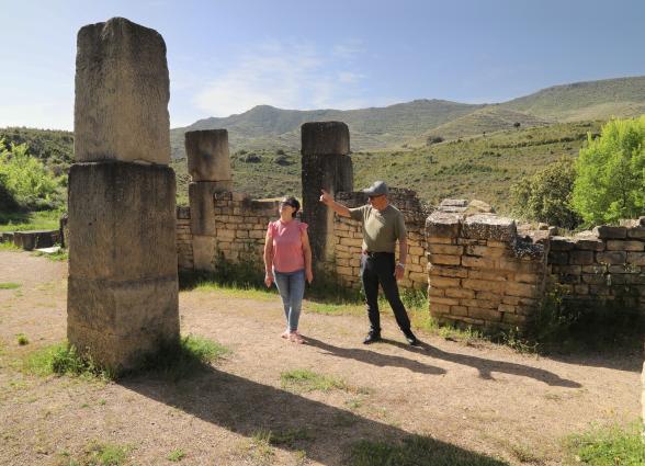 Yacimiento de Santa Criz de Eslava, con montañas verdes al fondo y visitantes explorando.