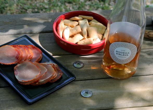 Degustación de productos locales en Bodega Eslava con lomo, pan y vino rosado sobre mesa de madera.