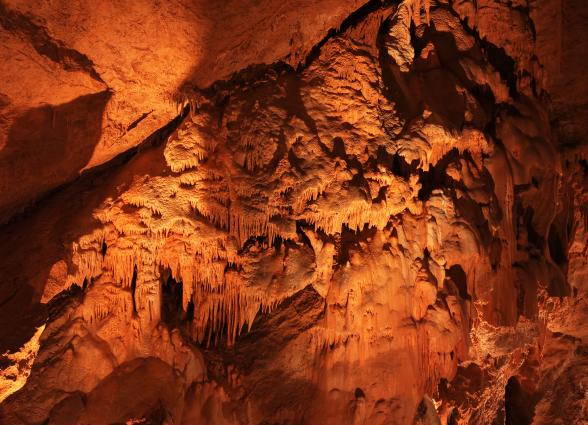 Cuevas de Mendukilo por dentro, con estalactitas y estalacmitas alumbradas con luces anaranjadas.