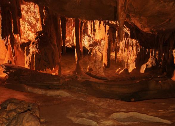 Cuevas de Mendukilo por dentro, con estalactitas y estalacmitas alumbradas con luces anaranjadas.