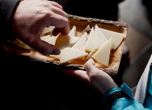 Manos de visitantes cogiendo queso cortado en experiencia Beloki Mendia, de Uztegui, Plazaola-Sakana-Ultzamaldea.