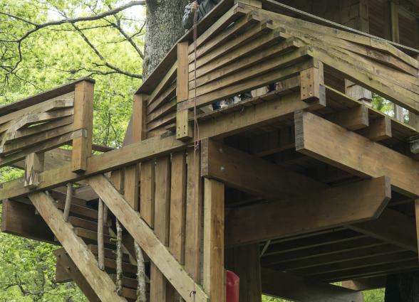 caleras y plataforma de madera, donde dos turistas suben una cesta de mimbre mediante una polea.