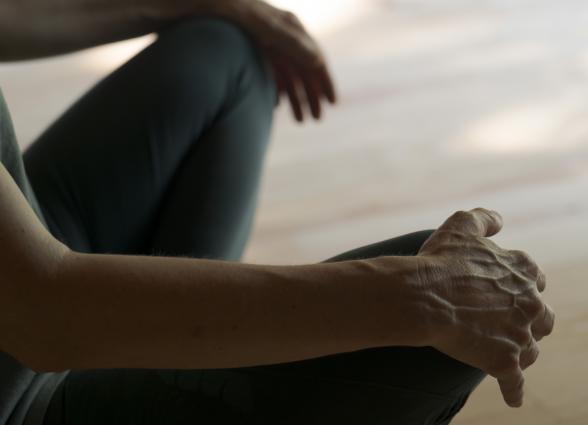 Detalle de manos sobre las rodillas de persona sentada practicando yoga en la experiencia de Ekino Aukera.