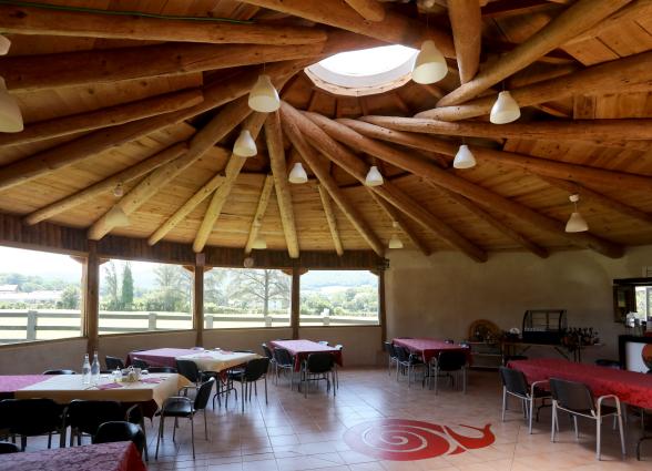 Interior de comedor con estructura de madera, mesas dispuestas y vistas al valle de Ultzama desde ventanales.