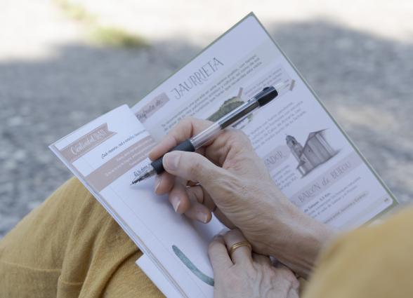 Mano sostiene libro de la experiencia de Karekin Kultura en Aoiz, detalle de persona escribiendo con portaminas.