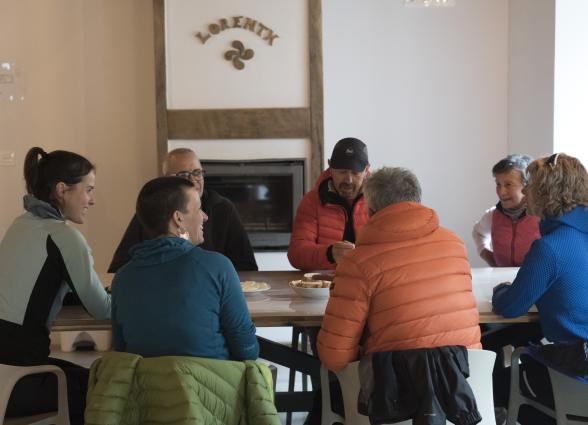 Grupo de visitantes en interior del albergue Lorentx, Pirineo Navarro, alrededor de mesa con comida local.