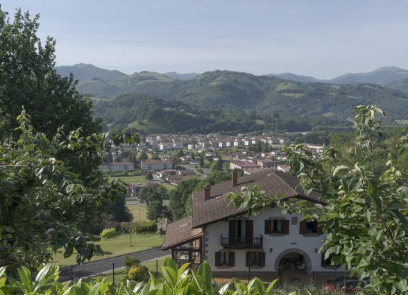 Vista panorámica del Valle de Baztan desde caserío tradicional con pueblo de Elizondo y montañas boscosas al fondo.