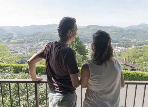huespedes contemplan el Valle de Baztan desde un balcon de Markulluko Borda, con pueblo de Elizondo y montes verdes al fondo.