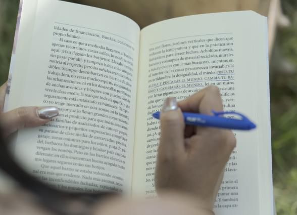 Mano sosteniendo boligrafo y libro abierto con texto subrayado de boli azul.