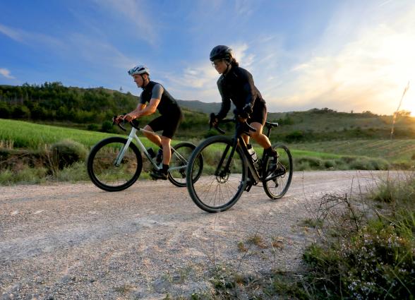 Dos ciclistas de gravel en ruta por Eslava, Comarca de Sangüesa, con paisaje prepirenaico con montes y río al fondo.