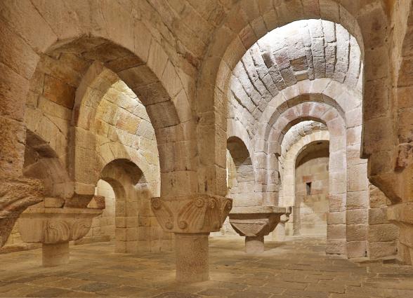 Interior de cripta románica con arcos de piedra y capiteles decorados en el Monasterio de Leyre.