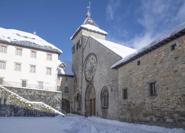 Iglesia Colegiata de piedra con campanario en Orreaga, rodeada de nieve invernal.