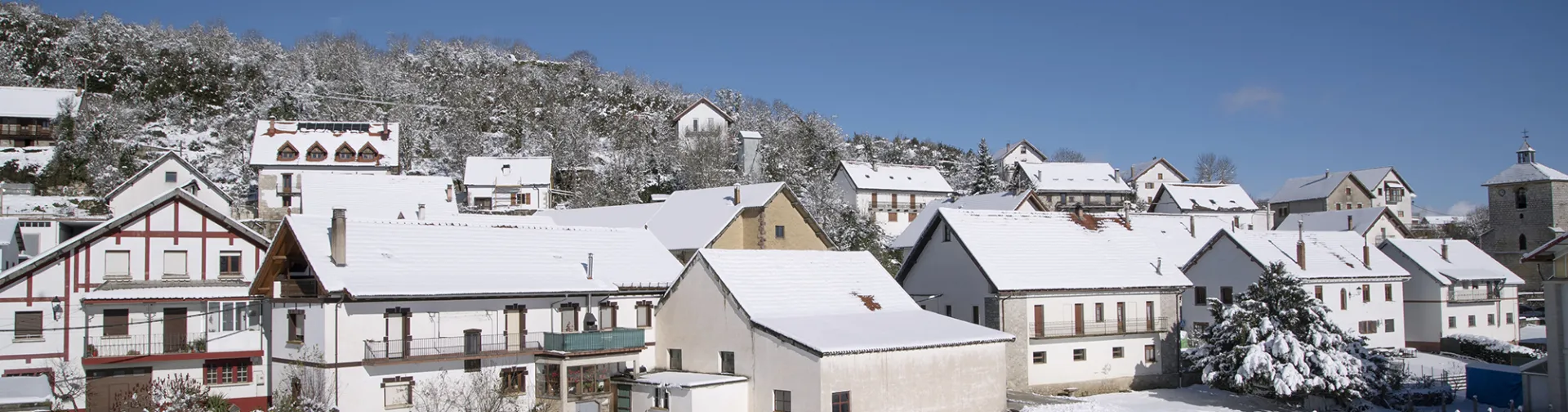 Casas tradicionales pirenaicas con fachadas blancas y tejados nevados en Abaurrea Alta, montes al fondo.
